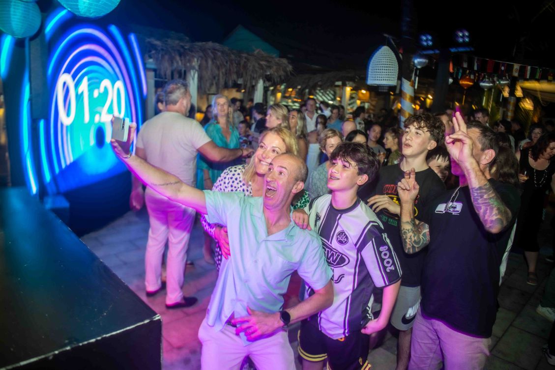 Guests gather at Shore Club An Bang Beach in Hoi An, excitedly preparing for the New Year's Eve countdown in front of a vibrant DJ setup and a large countdown screen.