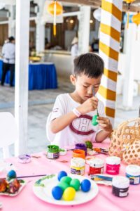 Child smiling while painting Easter eggs at Shore Club An Bang Beach during Easter Sunday celebrations.